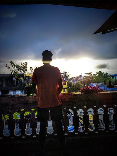 Rear view of man standing by bottles against sky during sunset