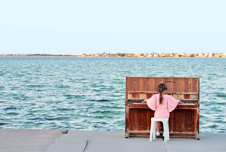 Little girl playing the old shabby piano wih sea background