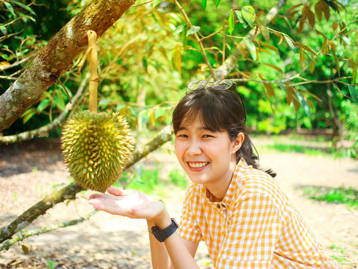 Portrait of smiling young woman showing fruit on tree