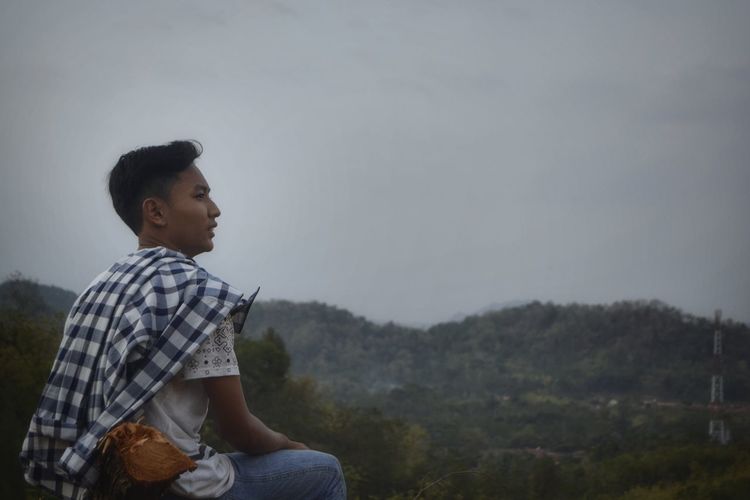 Side view of young man looking away against mountain