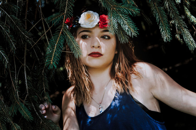 Beautiful young woman wearing flowers amidst branches