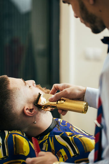 A barber cuts the beard of a man with a clipper in a barbershop