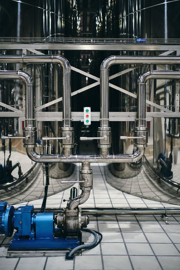 Metal pipes with control panel with buttons connected to steel tanks located in industrial area of contemporary plant