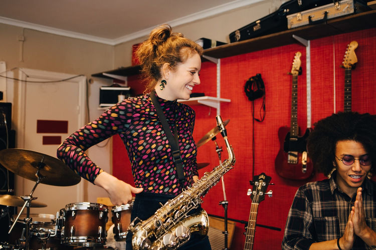 Smiling woman with saxophone standing by friend while practicing at recording studio