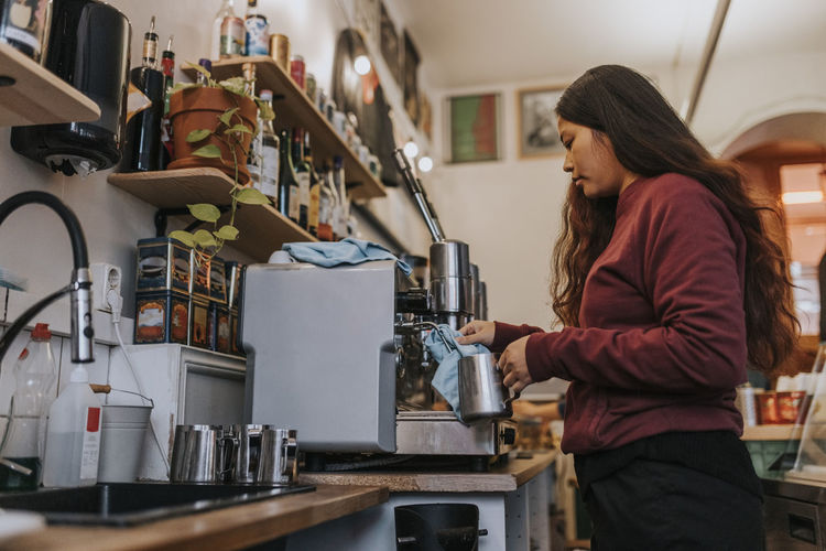 Side view of female entrepreneur making coffee in cafe