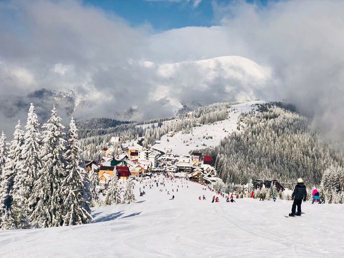 Skiers going down the slope on a sunny day with blue sky and fluffy clouds with view of mountains in 
