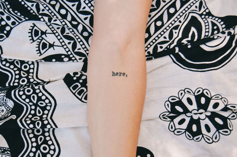 Cropped image of arm with tattoo on bed sheet