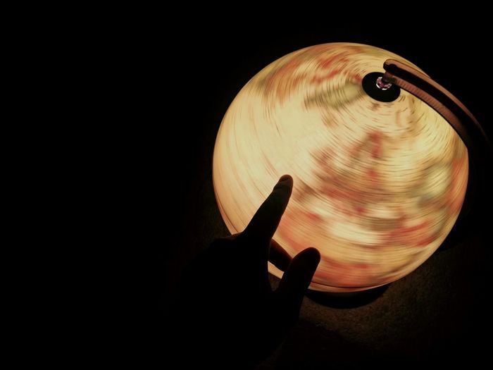 Cropped hand by illuminated globe in darkroom