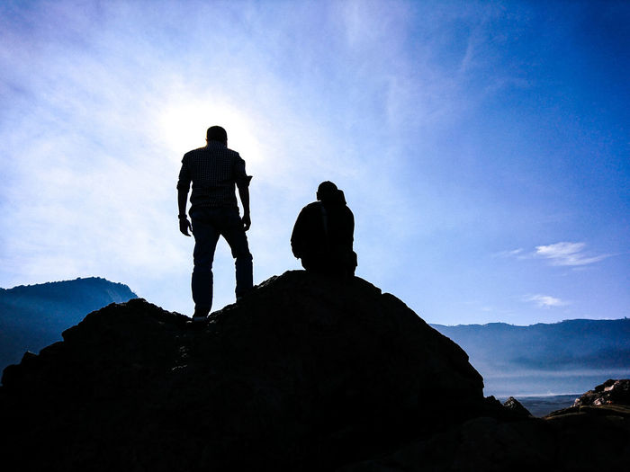 Low angle view of silhouette people standing on rock against sky