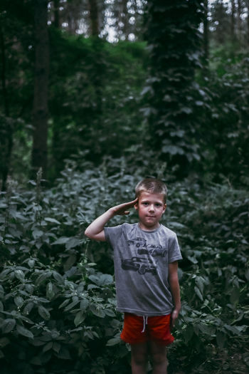 Portrait of cute boy saluting while standing in forest
