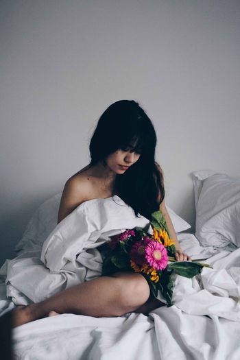 Naked woman with bouquet relaxing on bed at home