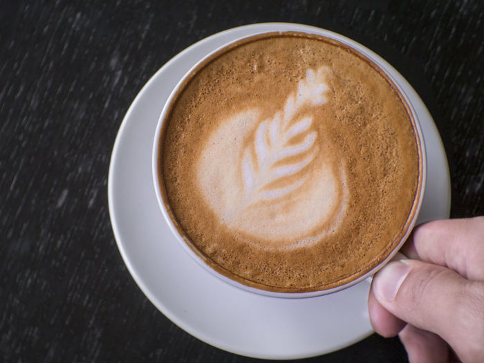 Close-up of hand holding cappuccino served on table