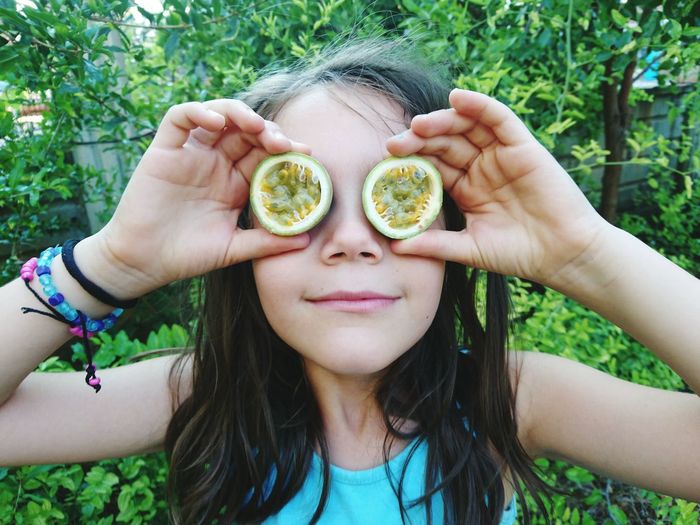 Smiling girl covering her eyes with sliced passion fruit