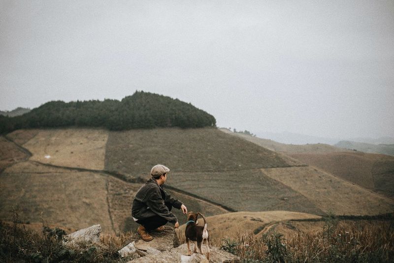 Man and his dog standing on land against sky
