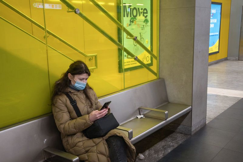 A young woman in a warm down jacket with green screen smartphone sits at subway