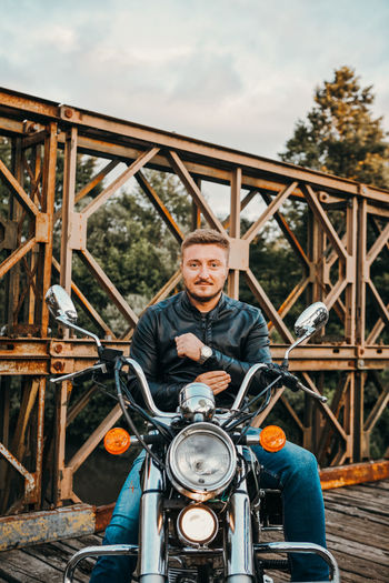 Portrait of man sitting on motorcycle over bridge