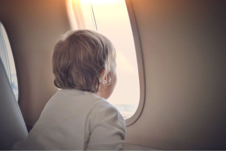 Rear view of boy looking through airplane window during sunset