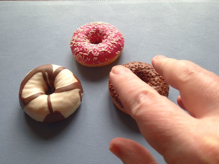 Close-up of cropped hand reaching towards donut on table