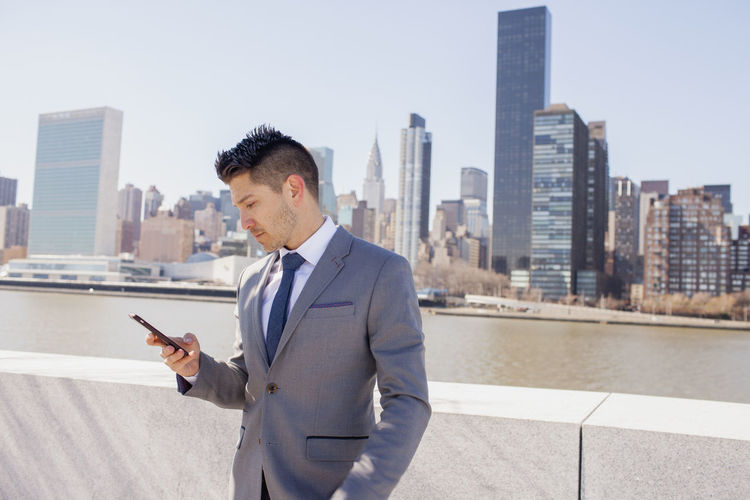 Portrait of a young businessman using his smartphone on a rooftop overlooking the city