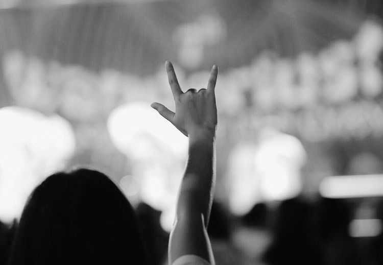Rear view of woman gesturing horn sign at music concert