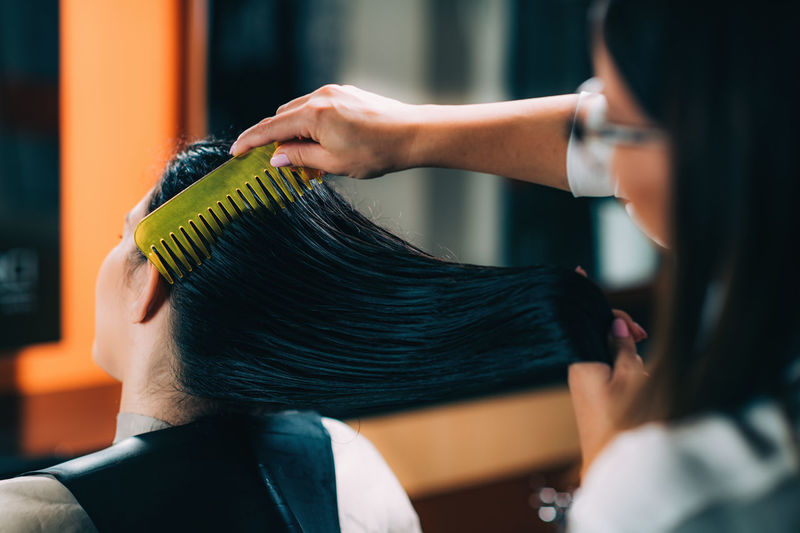Hairdresser combing customer hair in salon