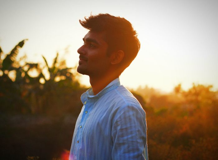 Young man standing against sky during sunset