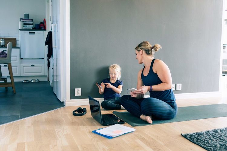 Daughter pointing at smart phone to mother while sitting on exercise mat at home