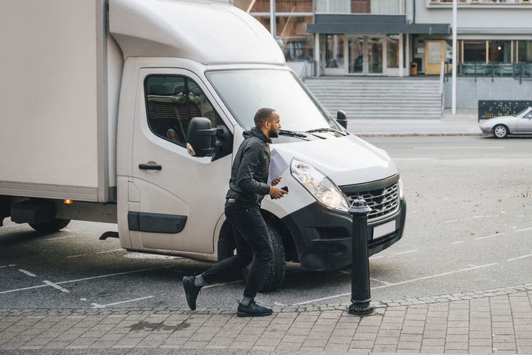 Male messenger with documents running by delivery van on street in city