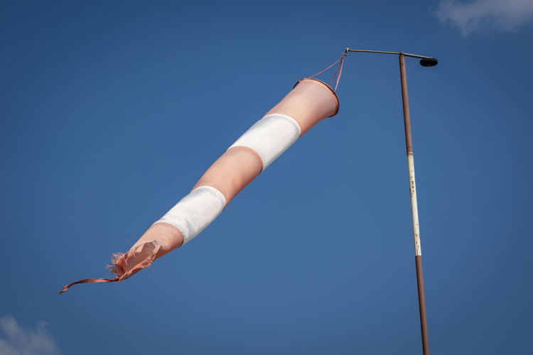 Low angle view of windsock pole against blue sky
