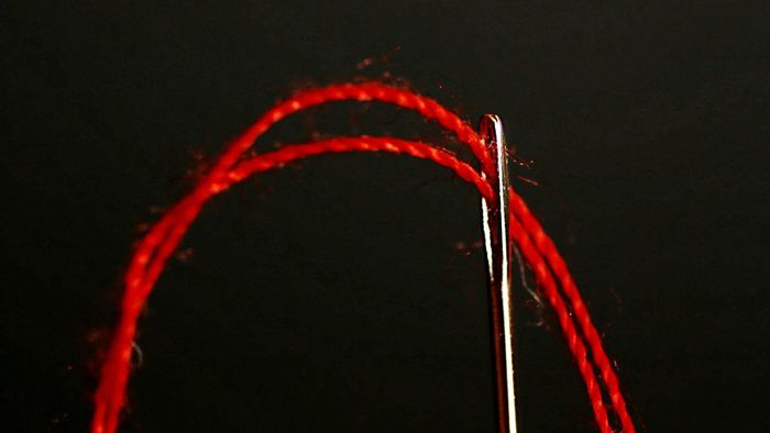 Close-up of red thread going through needle against black background