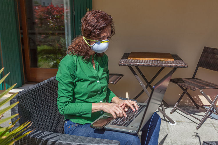 Woman with antivirus mask working with laptop in a garden. people life during the pandemic