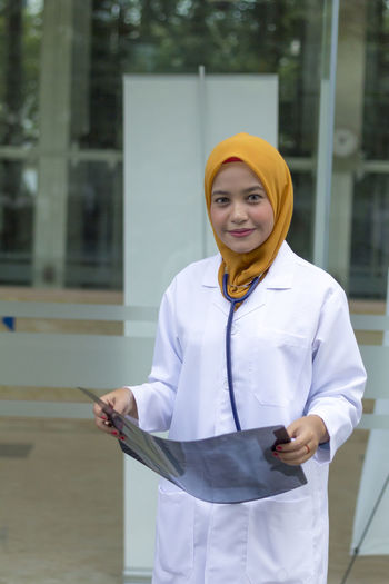 Portrait of female doctor holding x-ray while standing outside hospital