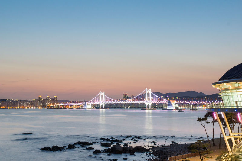 Illuminated bridge over river against sky at dusk