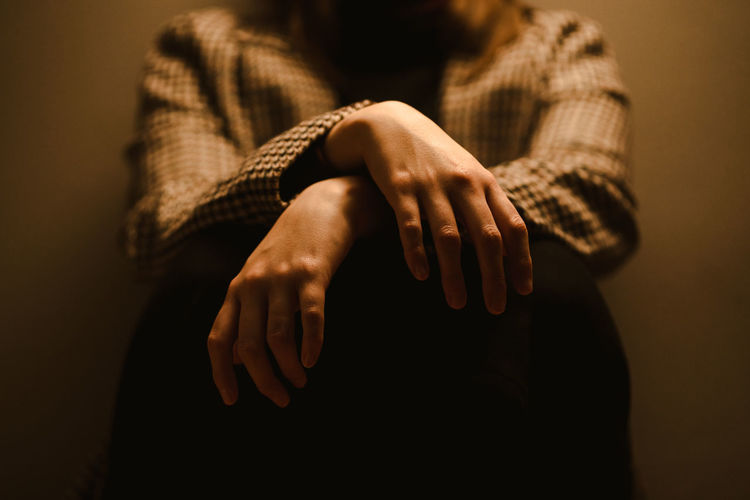 Selective focus of hands of crop anonymous exhausted depressive unhappy woman in checkered coat sitting in dark studio