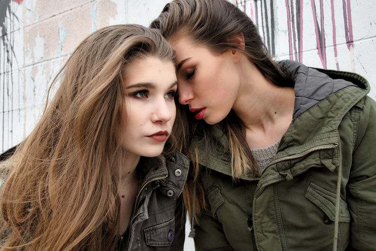 Close-up of female friends wearing warm clothing against wall