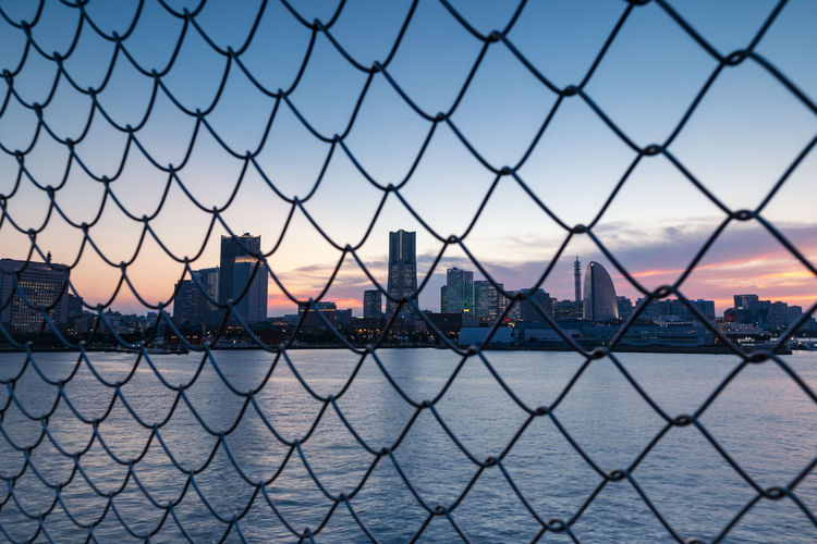 Cityscape by the sea through the grid of fence during sunset. selective focus.