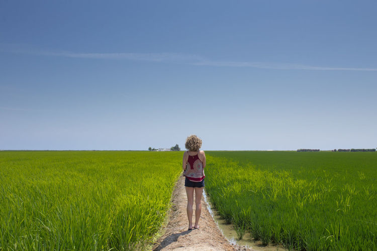 Rear view of woman walking on field against sky