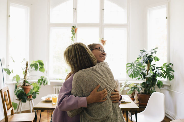 Parent embracing daughter while standing at home