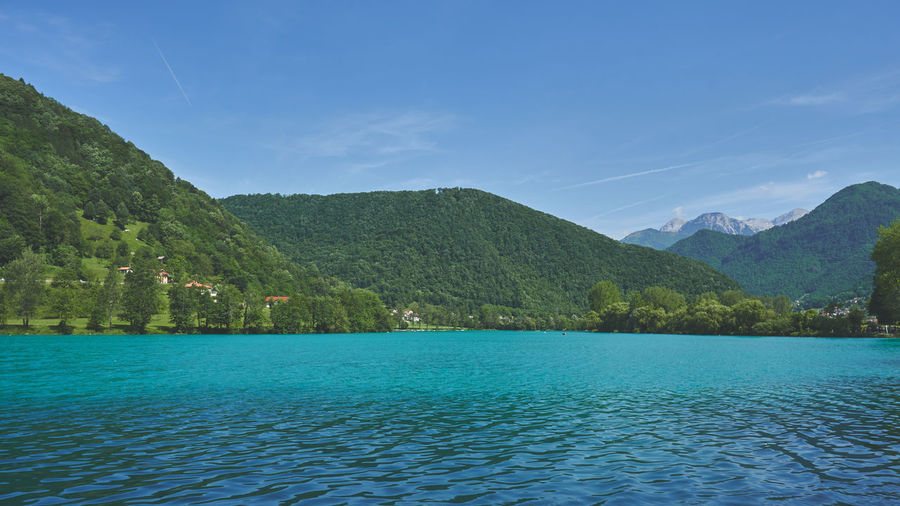 Scenic view of sea by mountains against blue sky