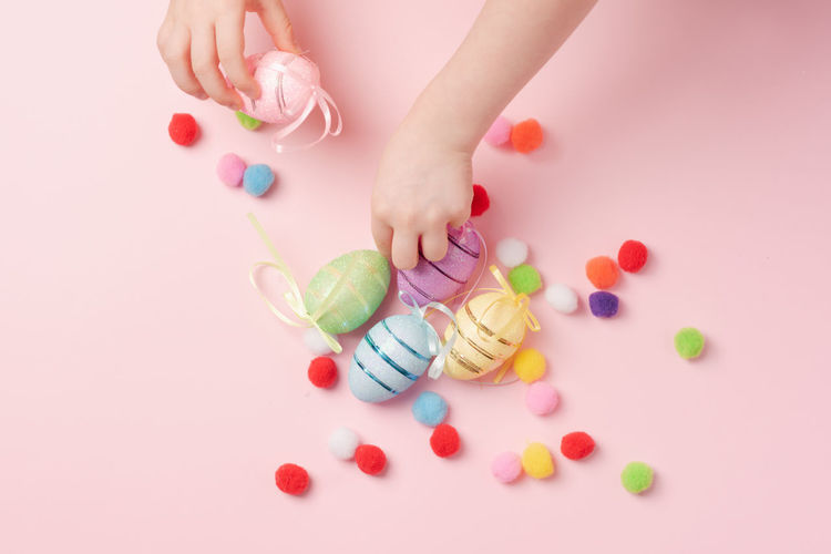 Cropped hand of child playing with pills against pink background