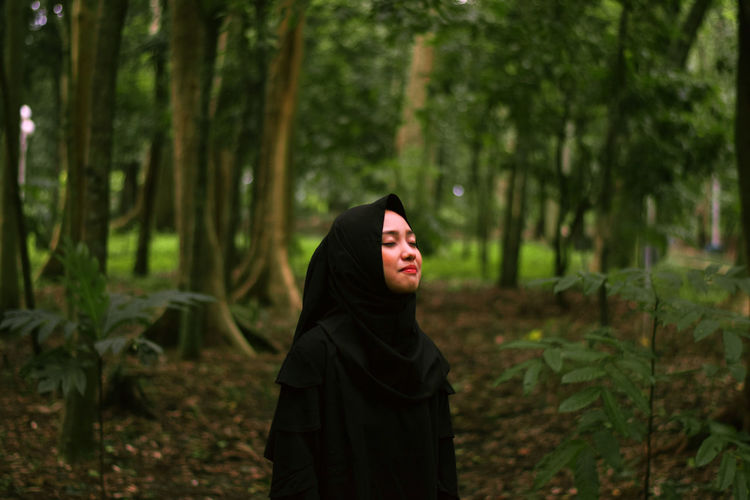 Woman with eyes closed standing against trees in forest