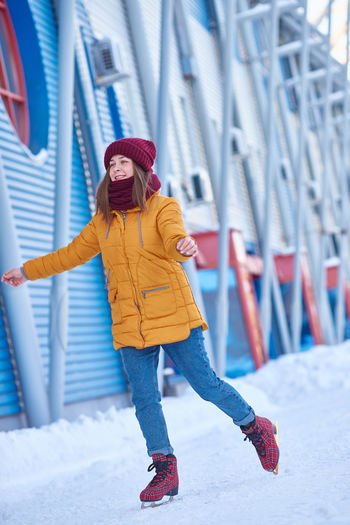 Young woman in a red hat and a yellow jacket is ice skating at the stadium on a frosty winter day. 