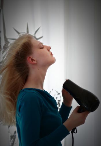 Side view of woman with hair dryer at home