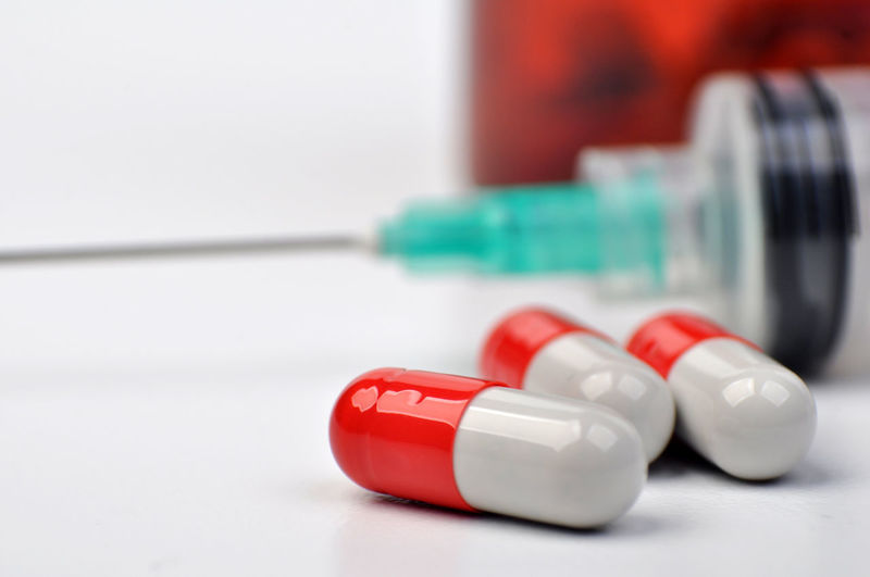 Close-up of capsules with syringe on white background