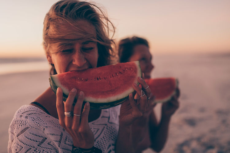 Women eating watermelon at beach during sunset