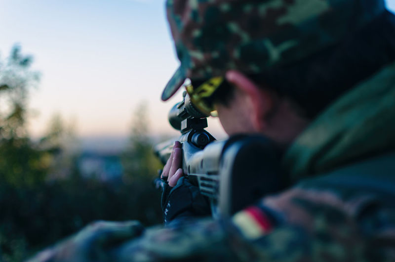 Close-up of army soldier aiming with sniper during sunset