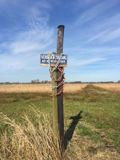 Sign on wooden post on field against sky