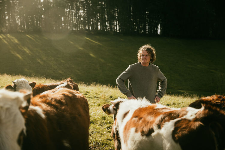Side view of man standing on field with his cows 