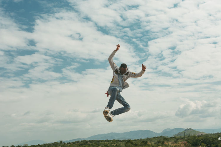 A man jumping on top of a hill against clouds and sky