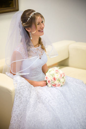 Bride holding bouquet while sitting on sofa